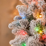 Close-up of flocked branches, pinecones and multicolor lights