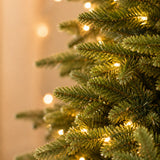 Close-up of lifelike green branch tips and warm white LED Christmas lights