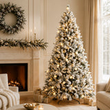 Snow-flocked artificial Christmas tree beside a holiday fireplace